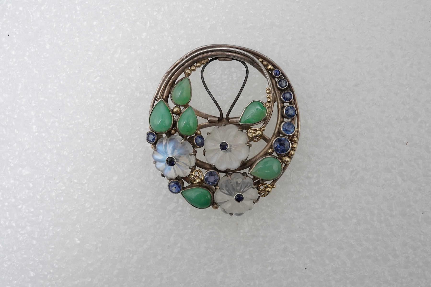 Attributed to Dorrie Nossiter (1893-1977), an Arts & Crafts moonstone, sapphire and jadeite scarf clip, 1920s